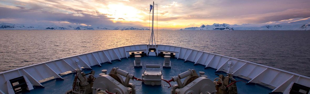 View from the bow of a ship onto the sea with a snow-covered coastline